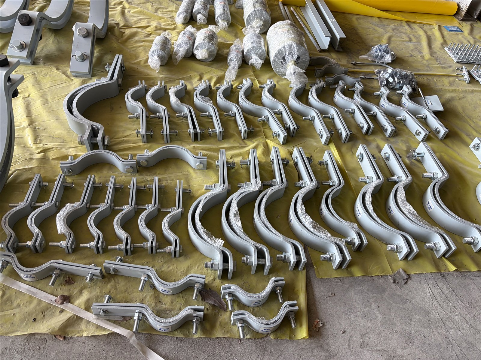 Rows of lined three-bolt pipe clamps with fasteners fitted, staged for a project order