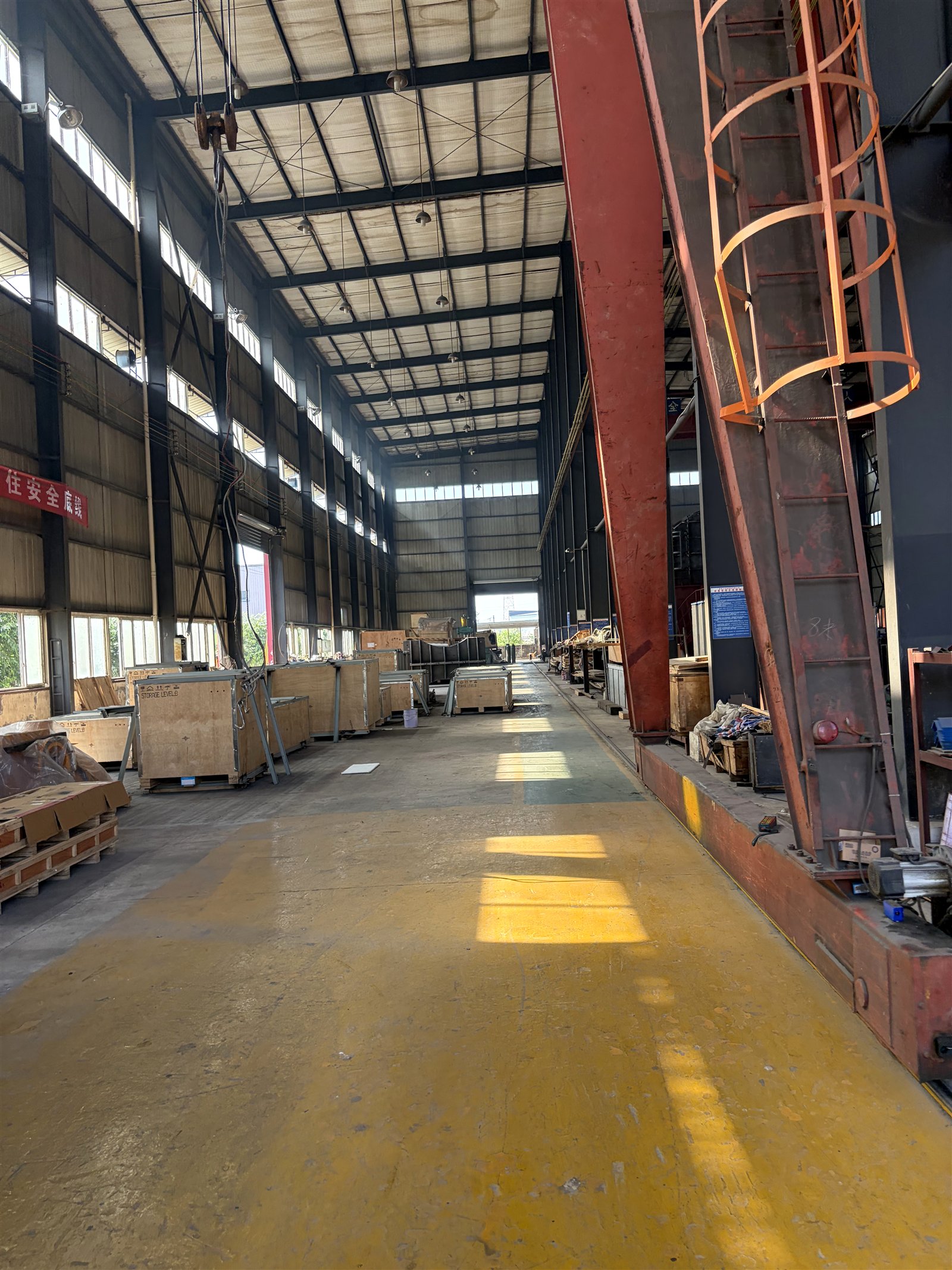 High-bay fabrication workshop with overhead lifting equipment, production aisle and packed components at the manufacturing base