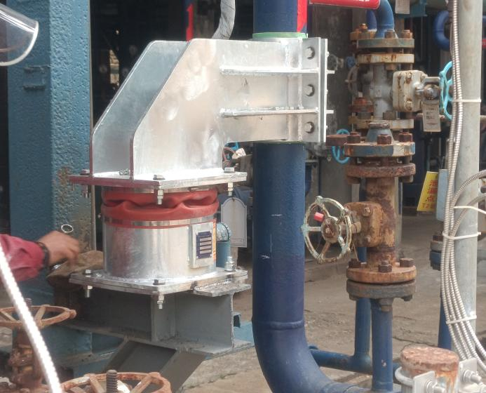 Field photo of a metallic installed assembly with bolted interfaces beside industrial pipework and valves; product identity is not established